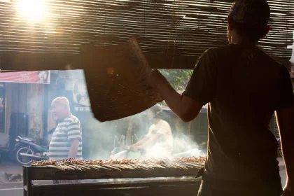 Photo of a man standing in front of a grill holding a newspaper, Indonesia, August 2014, Reinder Nijhoff