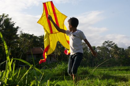Photo of a young boy holding a yellow and red kite, Indonesia, August 2014, Reinder Nijhoff