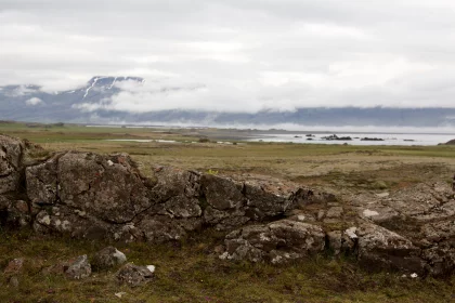 Photo of a rocky outcropping in a field with mountains in the background, Iceland, June 2016, Reinder Nijhoff