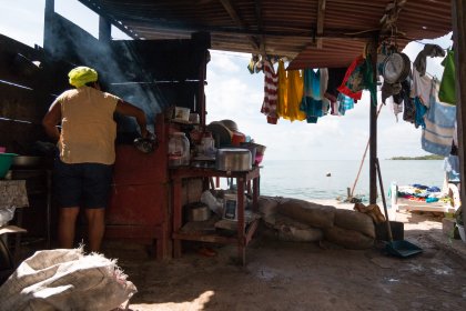 Photo of a man standing in front of a stove next to a body of water, Santa Cruz del Islote, Colombia, December 2017, Reinder Nijhoff