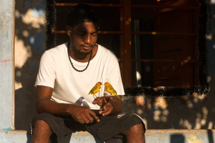 Photo of a man sitting on a ledge looking at his cell phone, Santa Cruz del Islote, Colombia, December 2017, Reinder Nijhoff