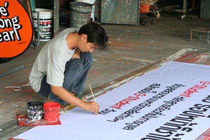 Photo of a man is painting a large sign on the ground, Thailand, Laos, Cambodja & Vietnam, November 2005, Reinder Nijhoff