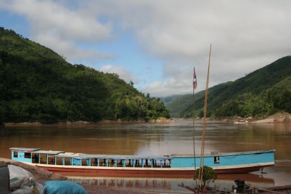 Photo of a blue boat sitting on top of a river next to a lush green hillside, Thailand, Laos, Cambodja & Vietnam, November 2005, Reinder Nijhoff