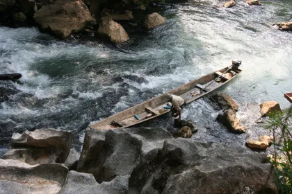Photo of a small boat sitting on top of a river next to rocks, Thailand, Laos, Cambodja & Vietnam, November 2005, Reinder Nijhoff