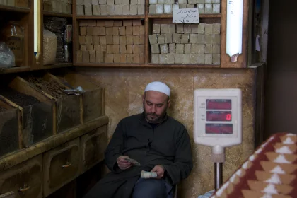 Photo of a man sitting in a room next to a scale, Jordan, Syria, Lebanon, May 2009, Reinder Nijhoff
