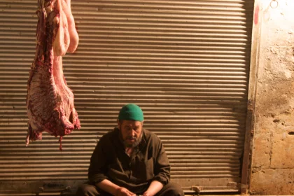 Photo of a man sitting on a bench in front of a meat hanger, Jordan, Syria, Lebanon, May 2009, Reinder Nijhoff
